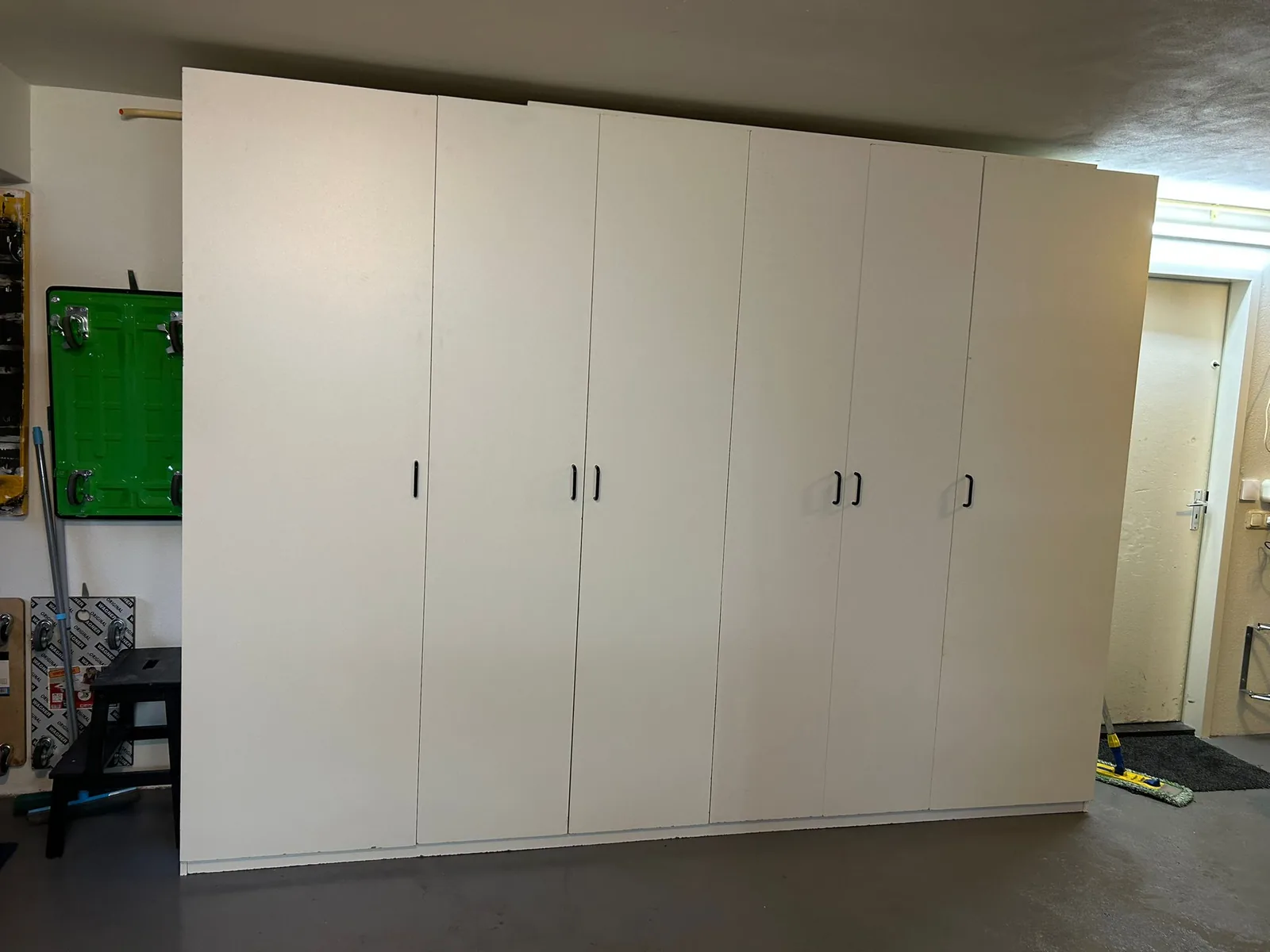 Een echte zelfgebouwde garagekast in wit melamine, van vloer tot plafond, met zes deuren en zwarte grepen